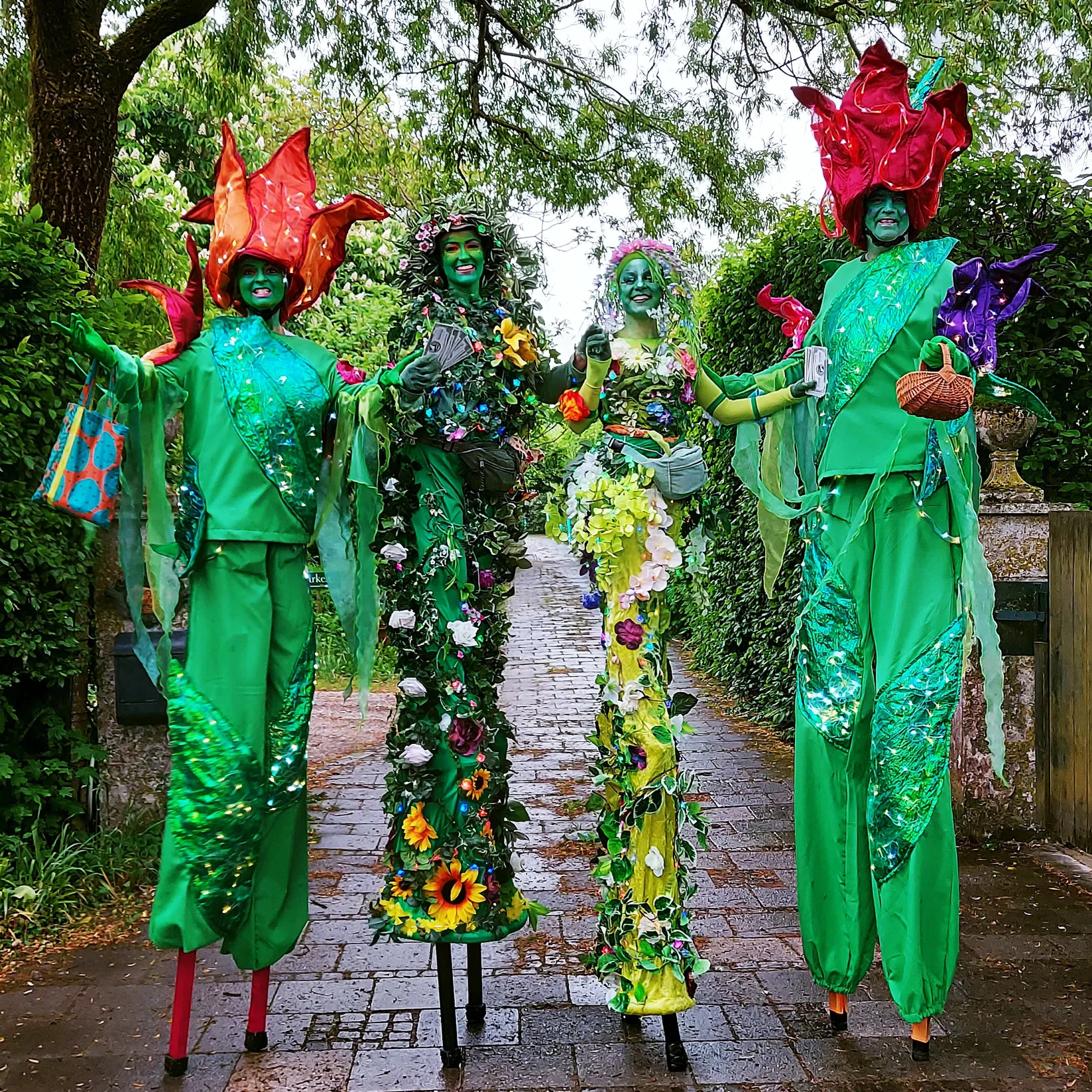 Vier Blumen auf Stelzen, Stelzengeher-Artisten von Williams Entertainment in bunten, blumigen Kostümen mit großen Blüten-Hüten