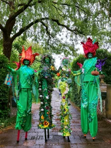 Vier Blumen auf Stelzen, Stelzengeher-Artisten von Williams Entertainment in bunten, blumigen Kostümen mit großen Blüten-Hüten